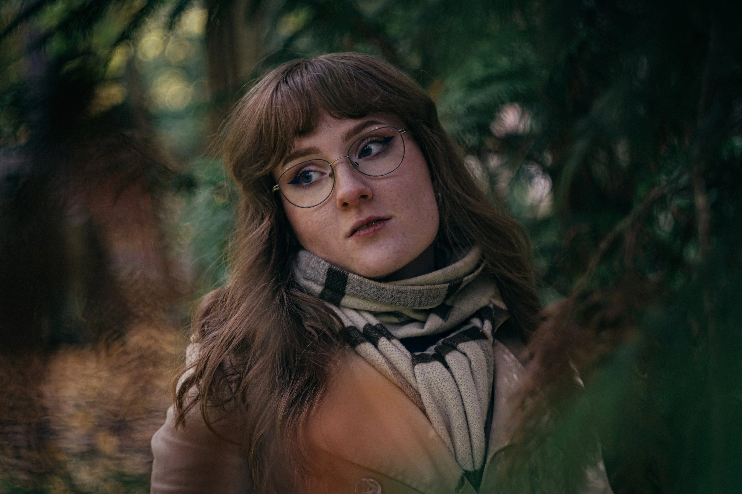 Junge Frau mit Brille und kariertem Schal in einem grünen Wald