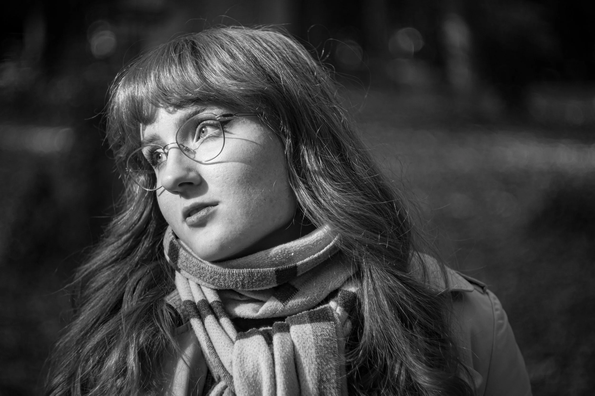 Schwarz-weiß-Foto eines jungen Mädchens mit Brille und Langhaar, das eine Strickschal trägt und in die Ferne schaut.