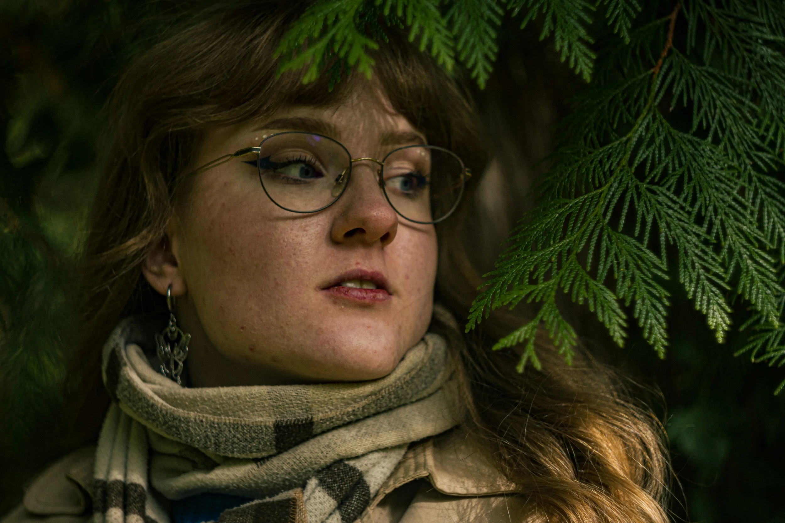 Nahaufnahme eines Mädchens mit Brille, das zwischen grünen Tannenzweigen liegt.