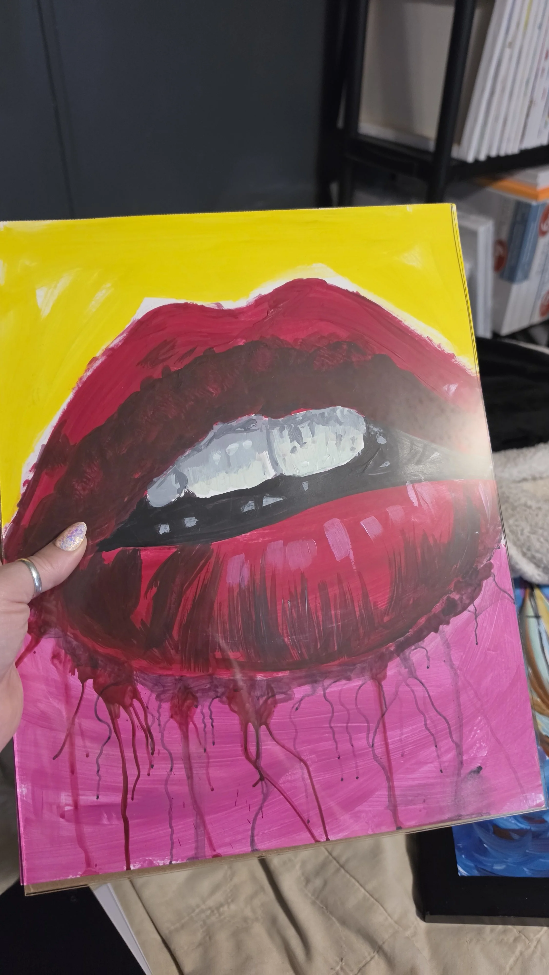 Close-up of a painted canvas depicting large red lips with exaggerated white teeth against a pink and yellow background. The lips appear to be painted in an expressive, artistic style with drips of paint.