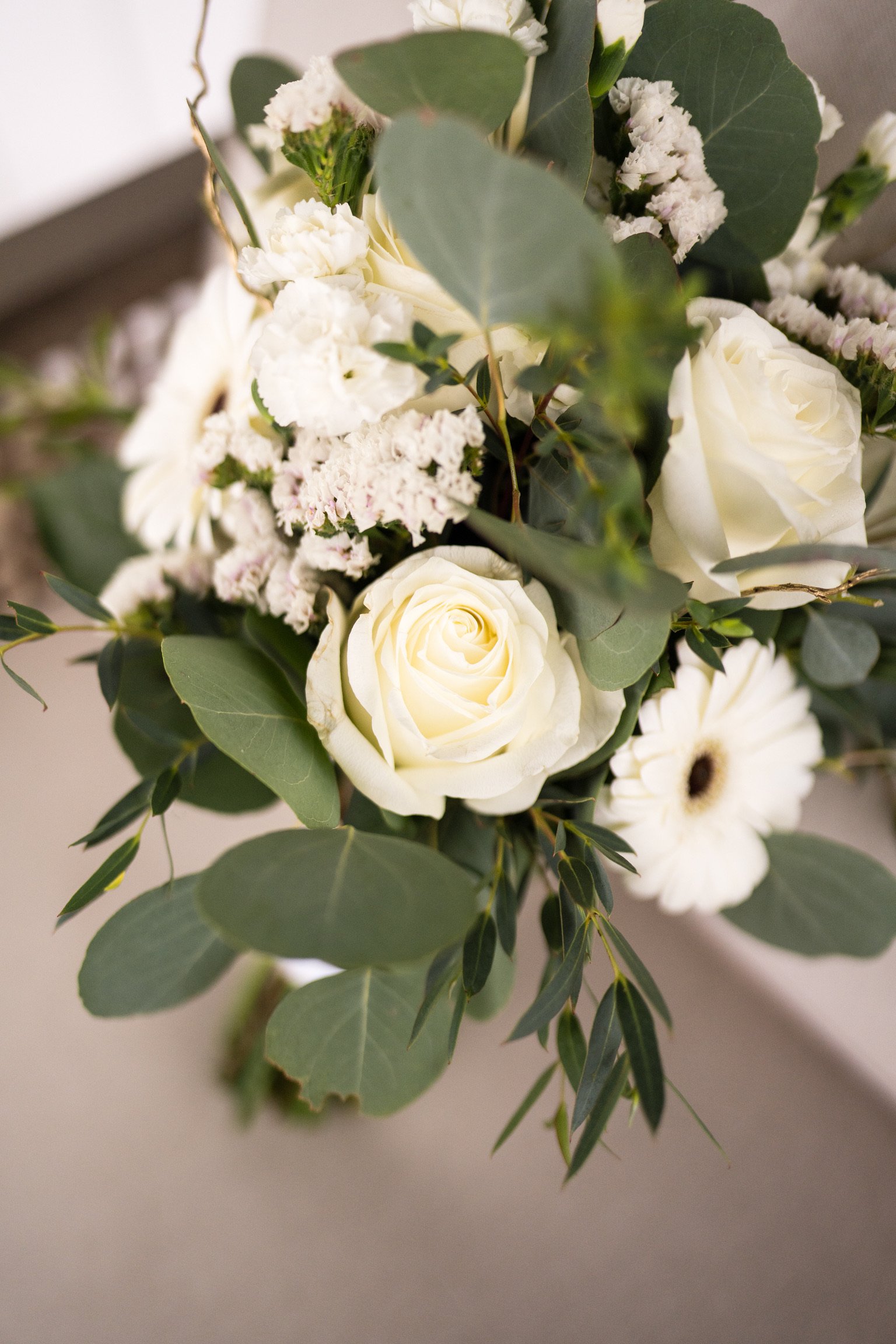 Close-up of a floral bouquet with white roses, white daisies, and greenery including eucalyptus leaves.