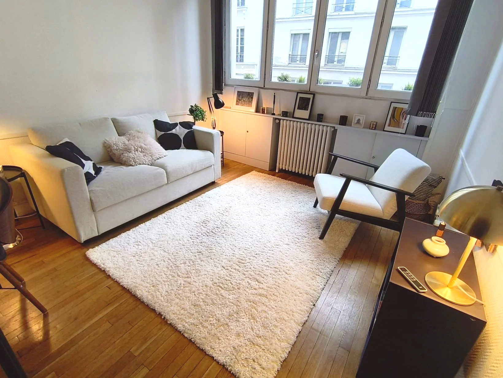 Salon moderne avec canapé blanc, tapis blanc, fauteuils, et grande fenêtre laissant entrer la lumière naturelle.