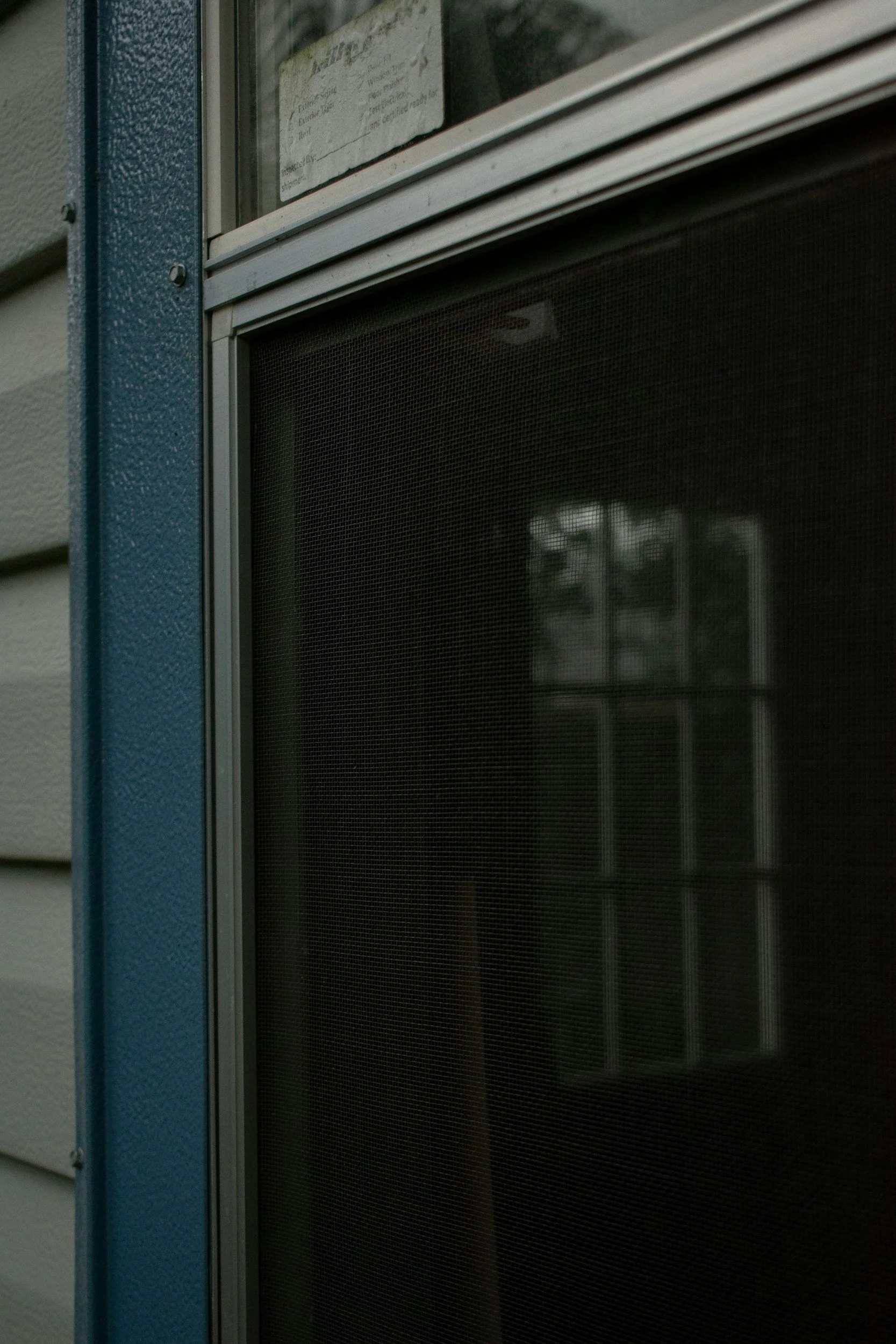 Close-up of a window screen with dark mesh and frame, viewed from outside