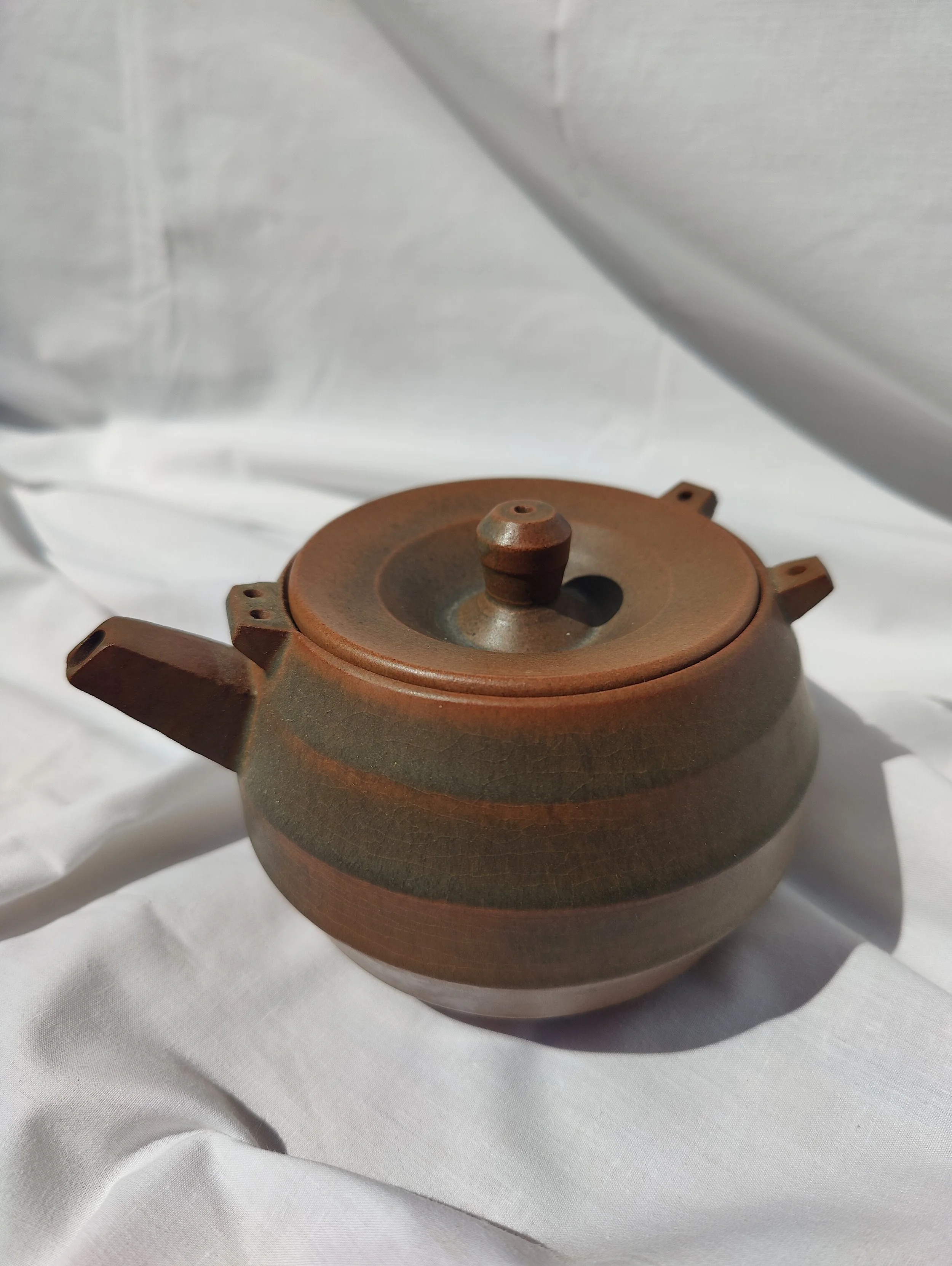 Tetera artesanal de ceràmica modelada al torn en tons marrons i teula amb orelletes per a nansa exterior, feta per Ceràmiques PasVi a La Bisbal d'Empordà.