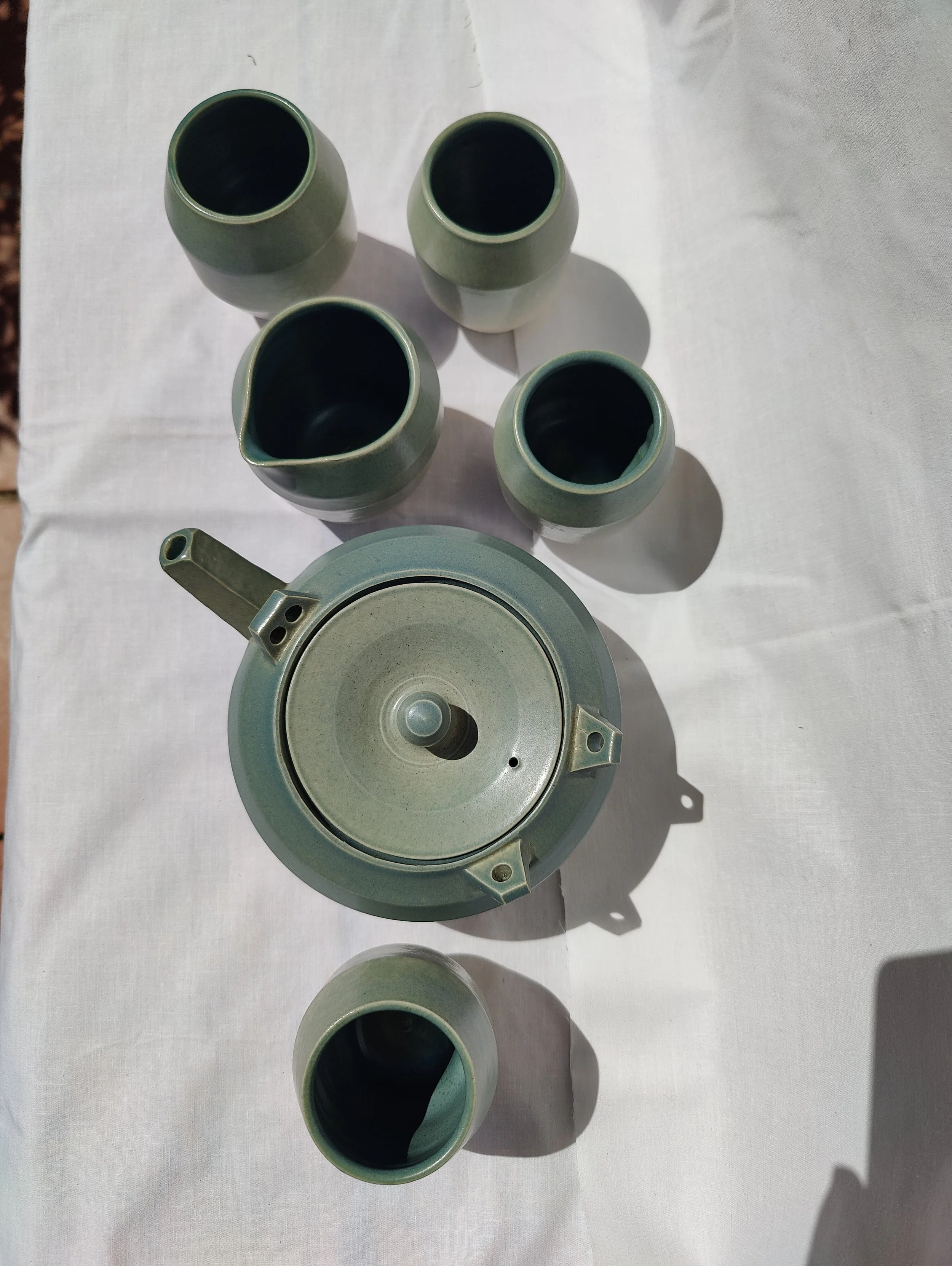Joc de te artesanal de gres blanc de la Bisbal, amb tetera, quatre gots i gerra de llet esmaltats en verd celadó, fet a mà al torn per Ceràmiques PasVi.