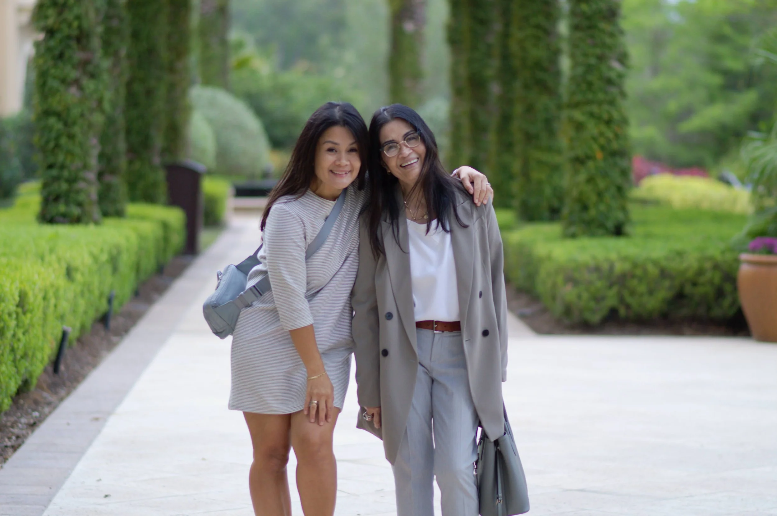 Two women smiling and hugging each other in a park with trees and grass in the background.