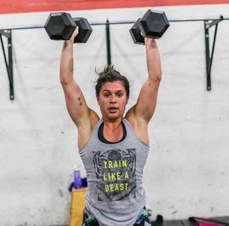 Woman lifting dumbbells overhead in a gym.
