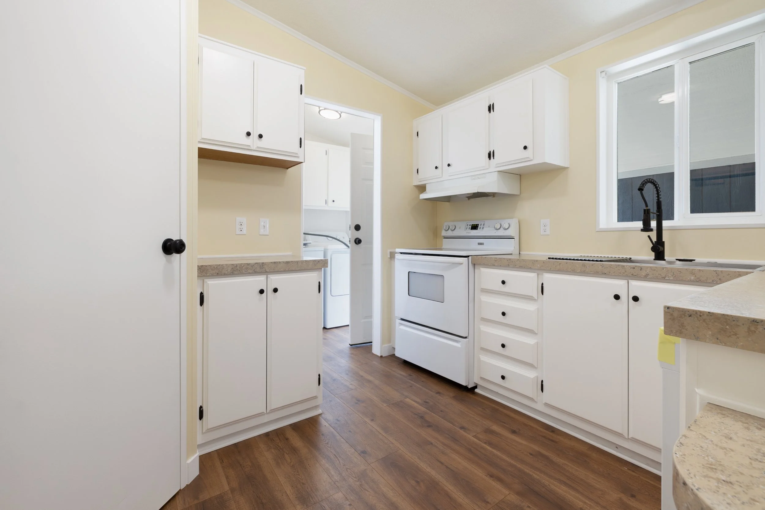 A kitchen with white cabinets, a stove, black faucet, and a window showing an outside view.