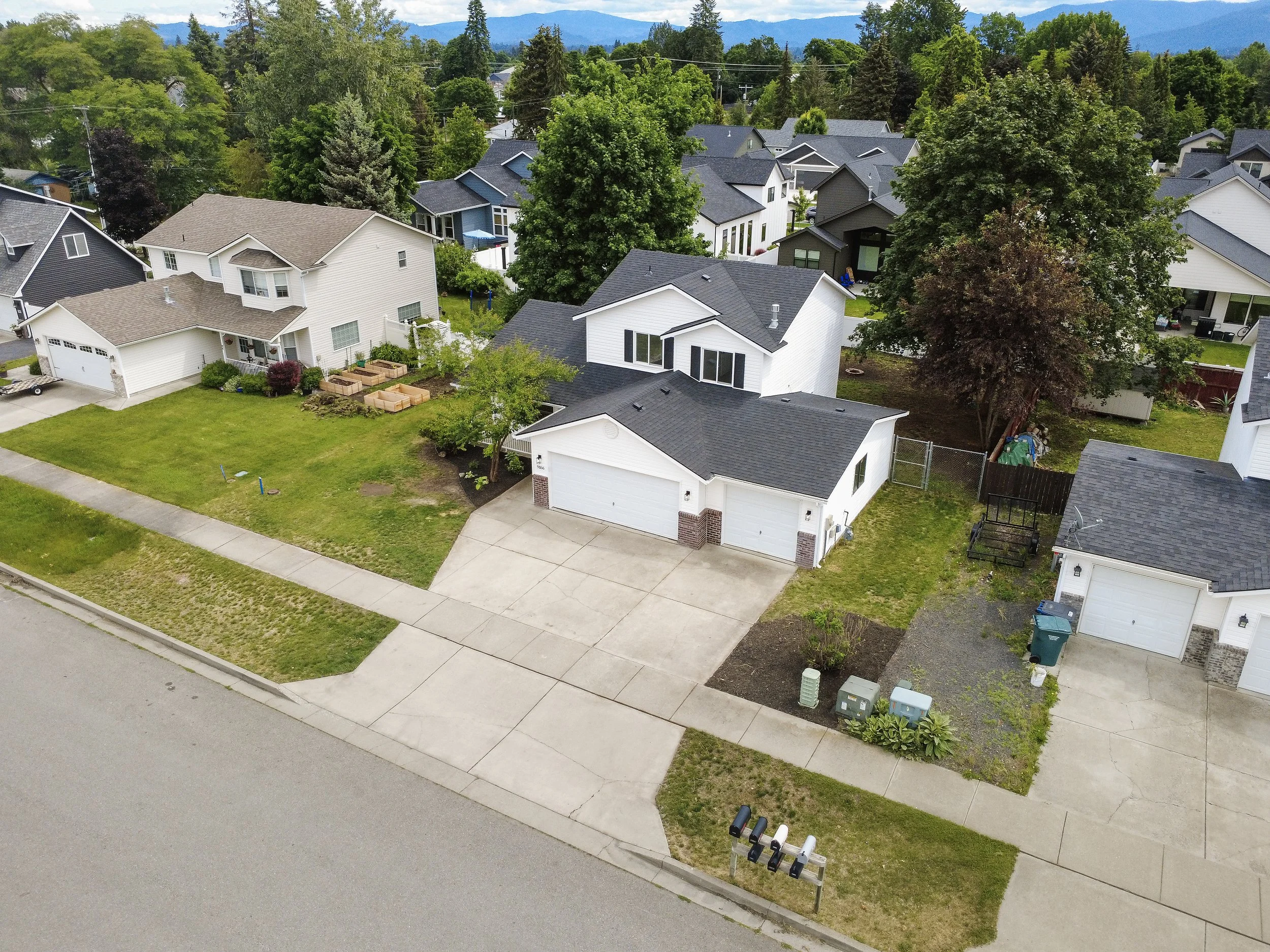 Aerial view of a suburban neighborhood with multiple modern houses, green trees, and mountain range in the background.