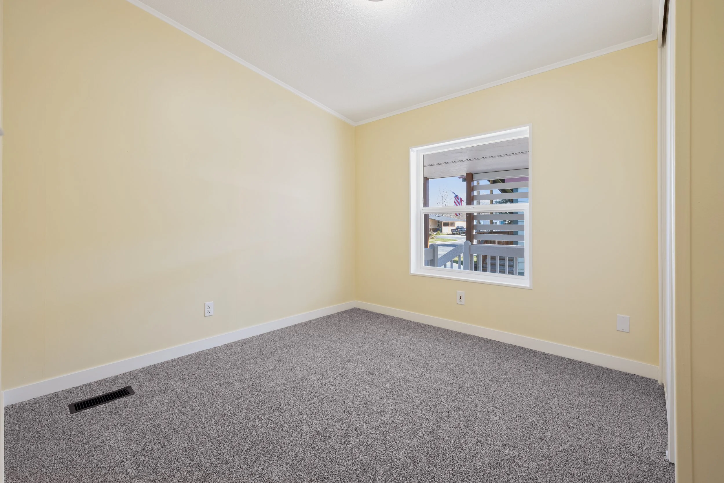 Empty room with yellow walls, a large window with blinds, and carpeted flooring.
