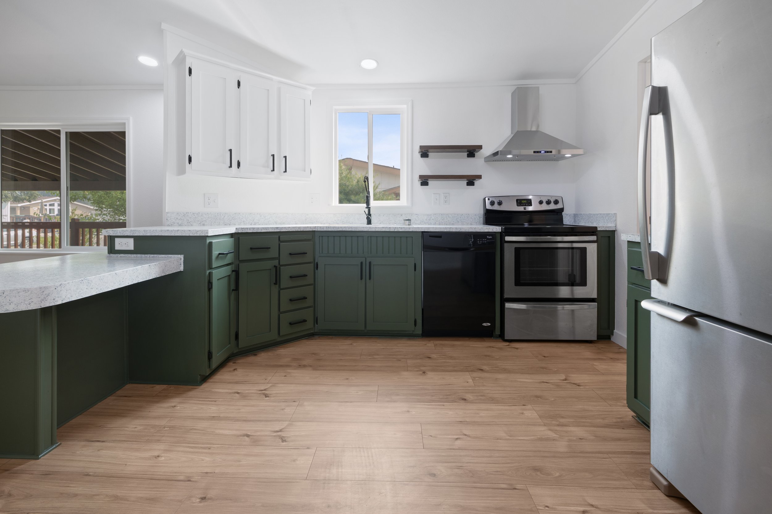 Modern kitchen with white cabinets, a window, stainless steel appliances, and light wood flooring.