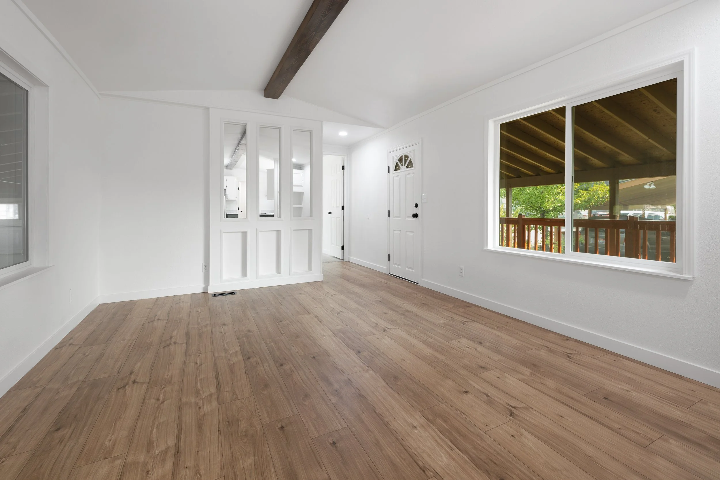 Empty room with white walls, large window, sliding door, and wooden flooring.