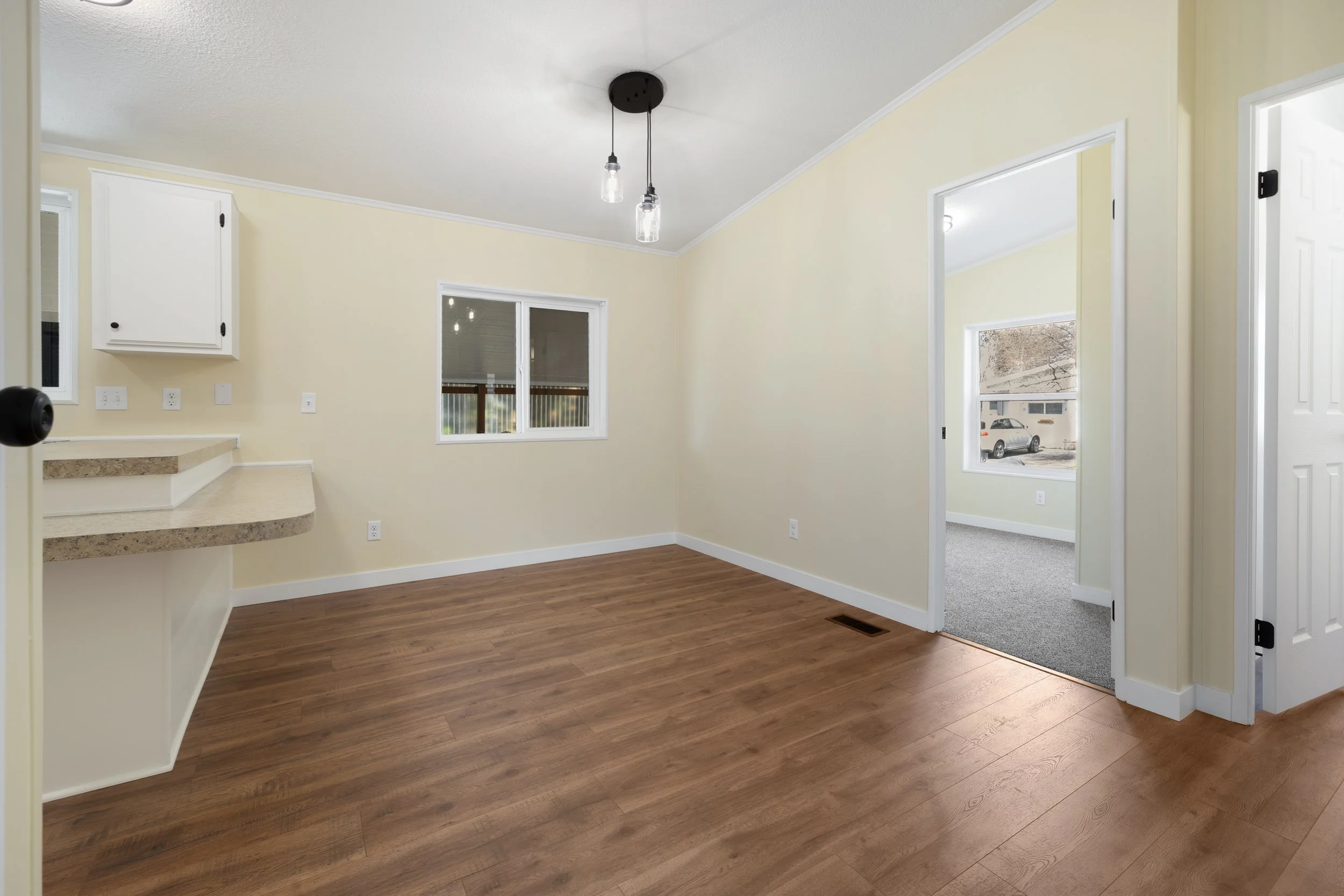 Interior view of a room with wood flooring, cream walls, a small window, and a ceiling light with two hanging bulbs.
