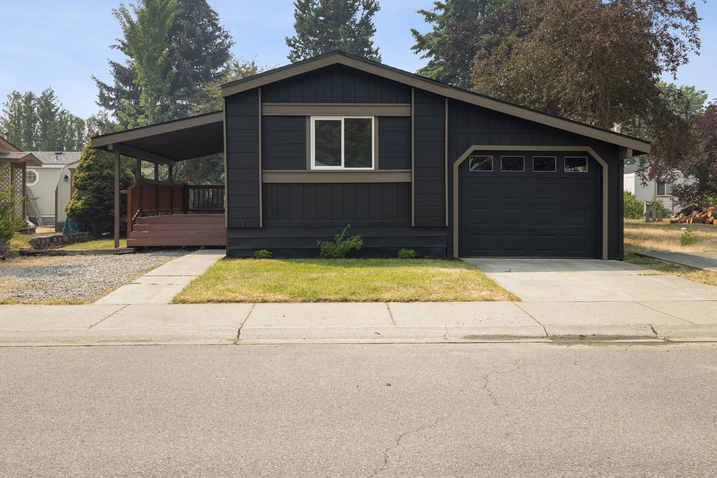 Front view of a black house with a garage, front lawn, sidewalk, and trees in the background.