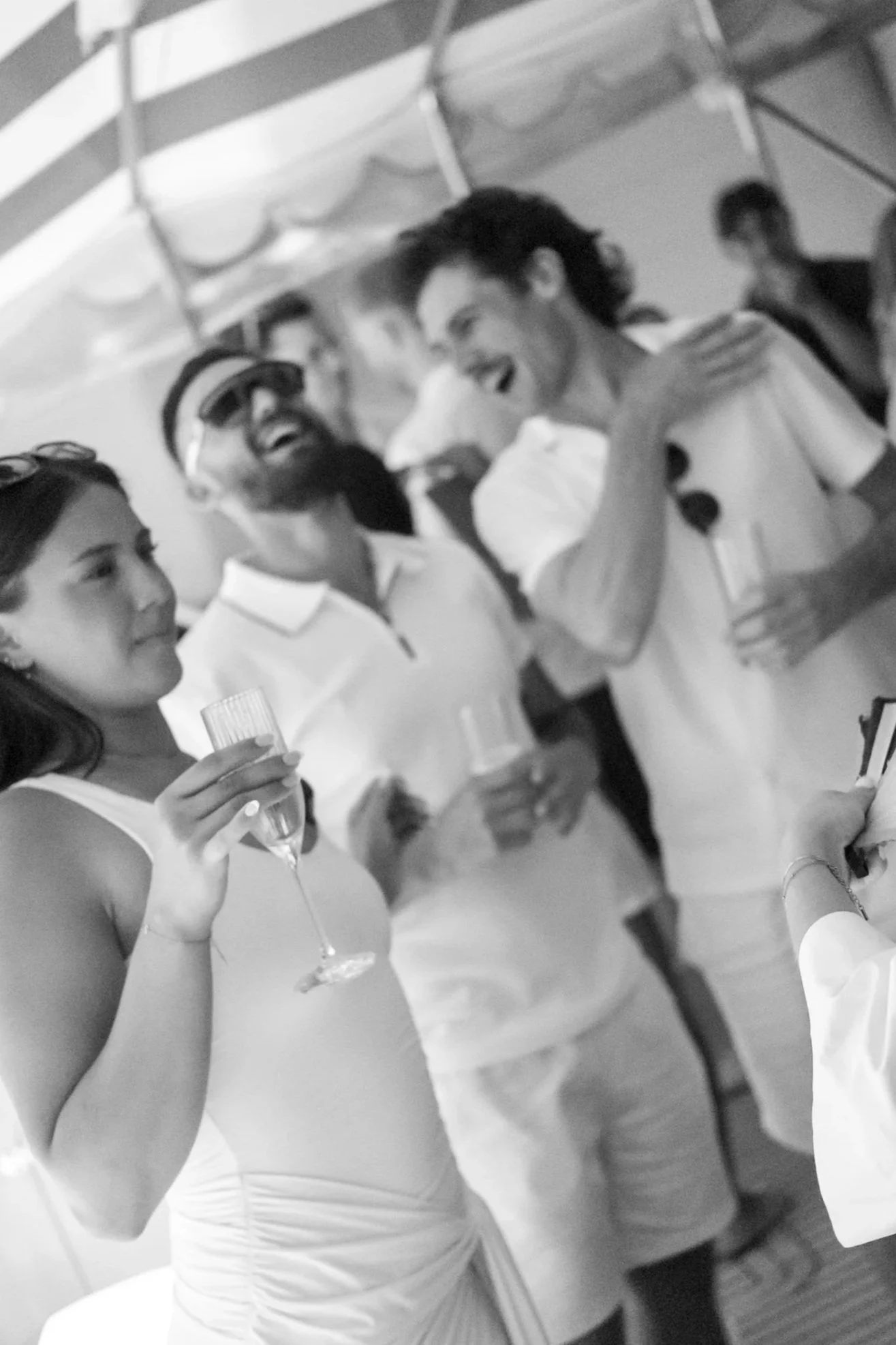 Black and white photo of a woman in a strapless dress holding a glass of champagne, talking to a group of friends at a celebration or party.