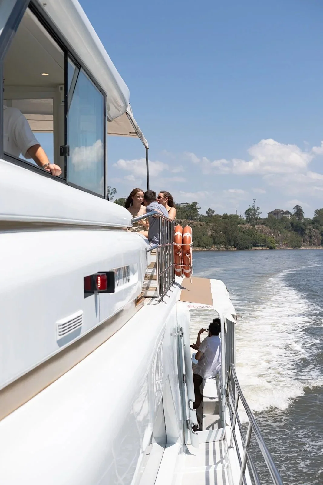 People enjoying a boat trip on a bright day, sitting on the deck with a view of the water and shoreline in the background.