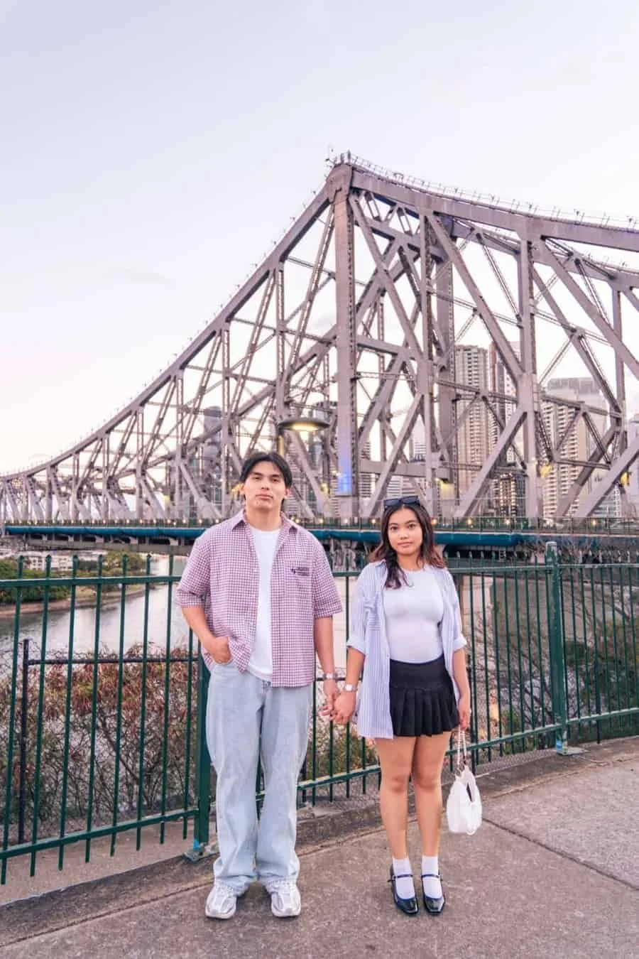 Couple holding hands on a bridge with Brisbane city buildings behind them