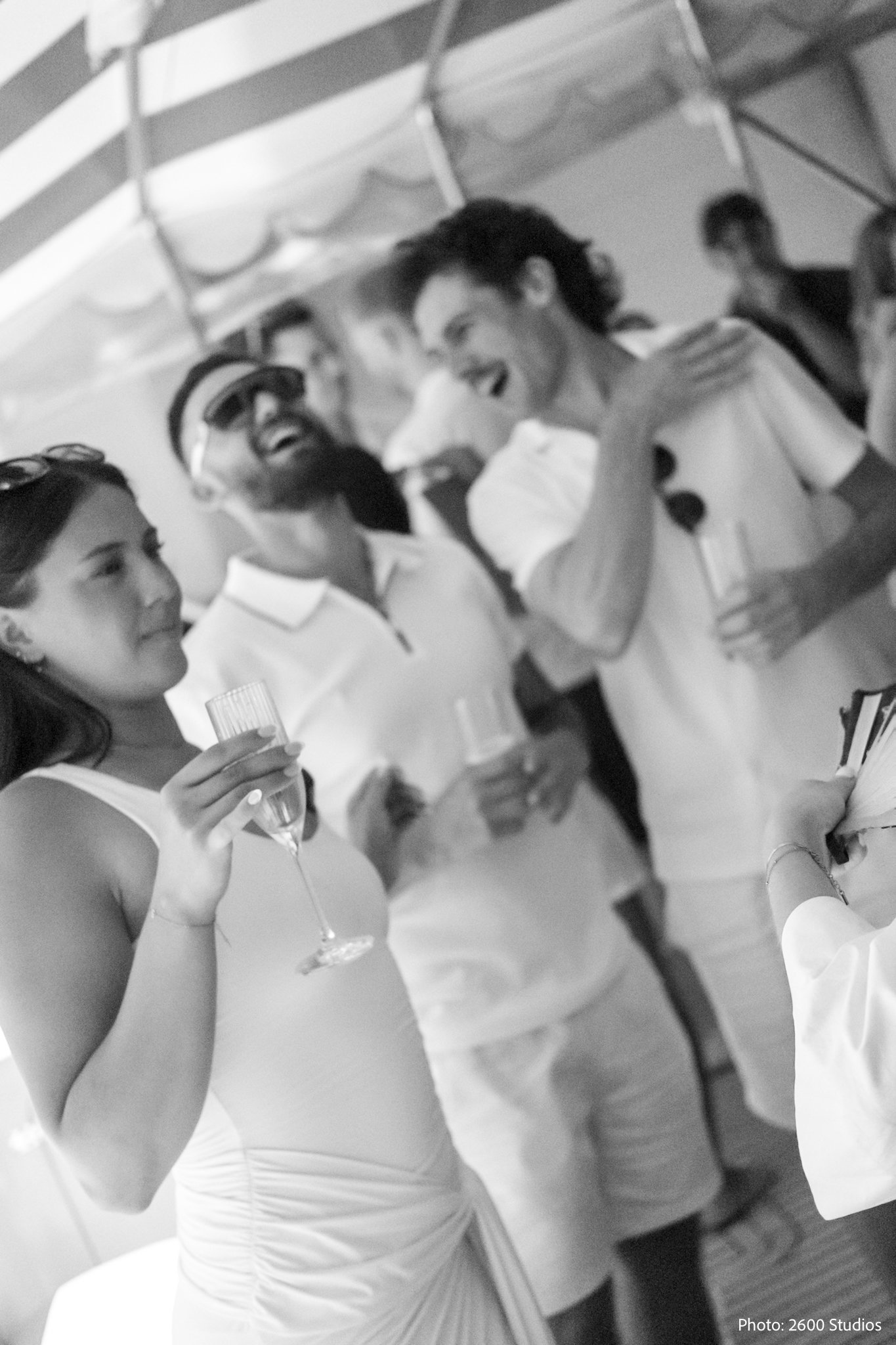 Black and white photo of elegantly dressed guests in white attire enjoying champagne at an outdoor summer party.