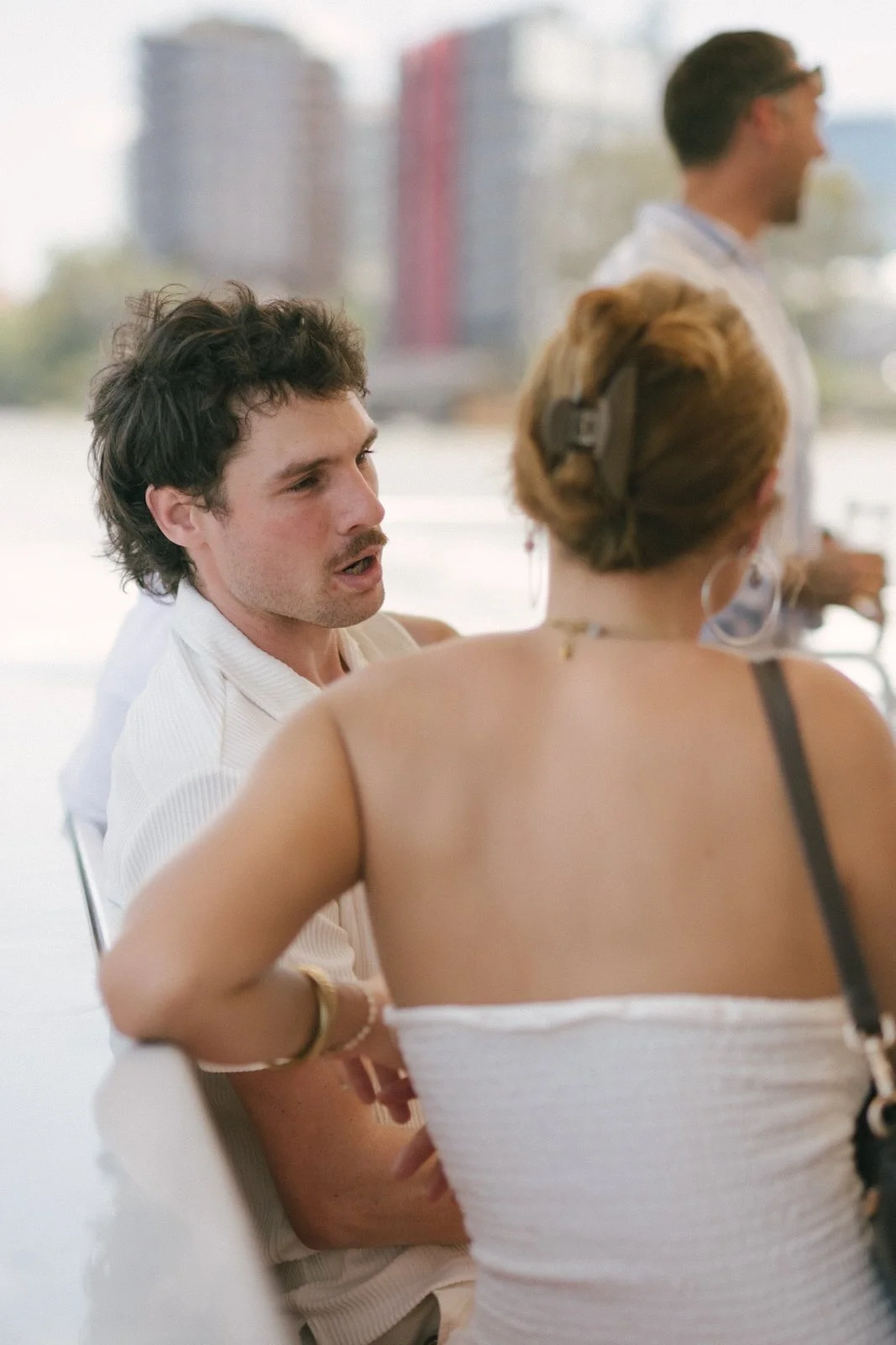A man and woman are engaged in a conversation at a social event, with another man in the background.