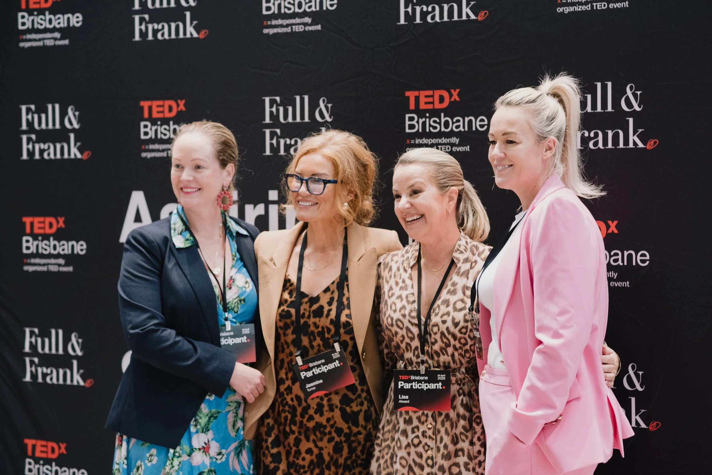 Four women standing together at a TEDx Brisbane event, smiling and shaking hands, with a black backdrop featuring TEDx Brisbane and Full & Frank logos.