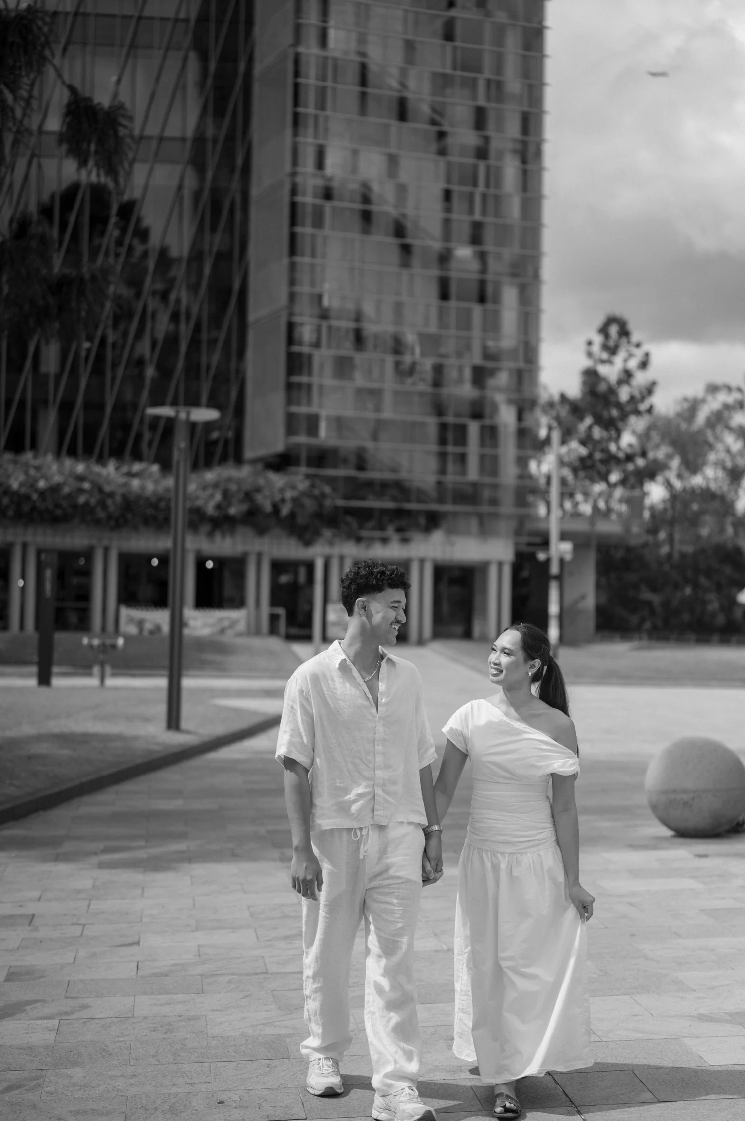 Engaged couple holding hands and smiling while walking near Brisbane Parliament House
