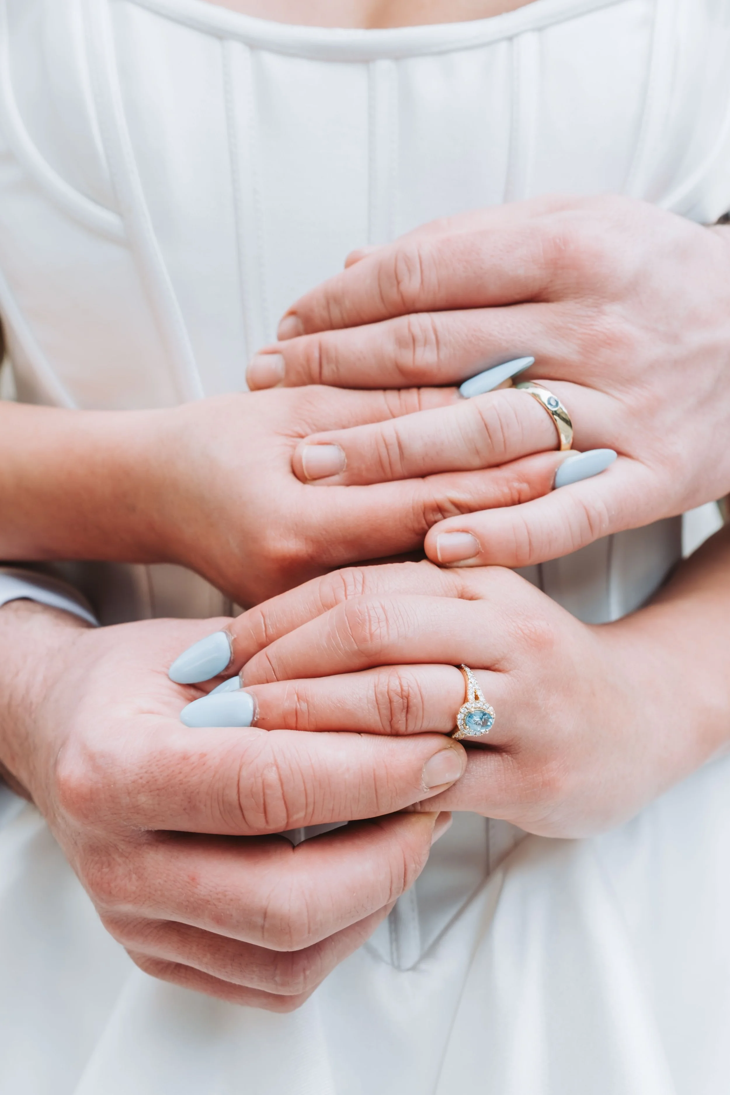 Close-up of two hands with rings, one on top of the other, with a white fabric background.