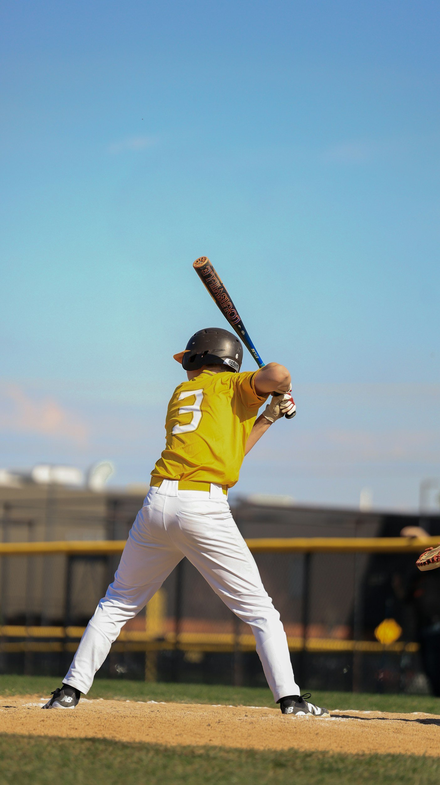A baseball player in a yellow jersey and white pants is swinging a bat at a baseball game on a sunny day.