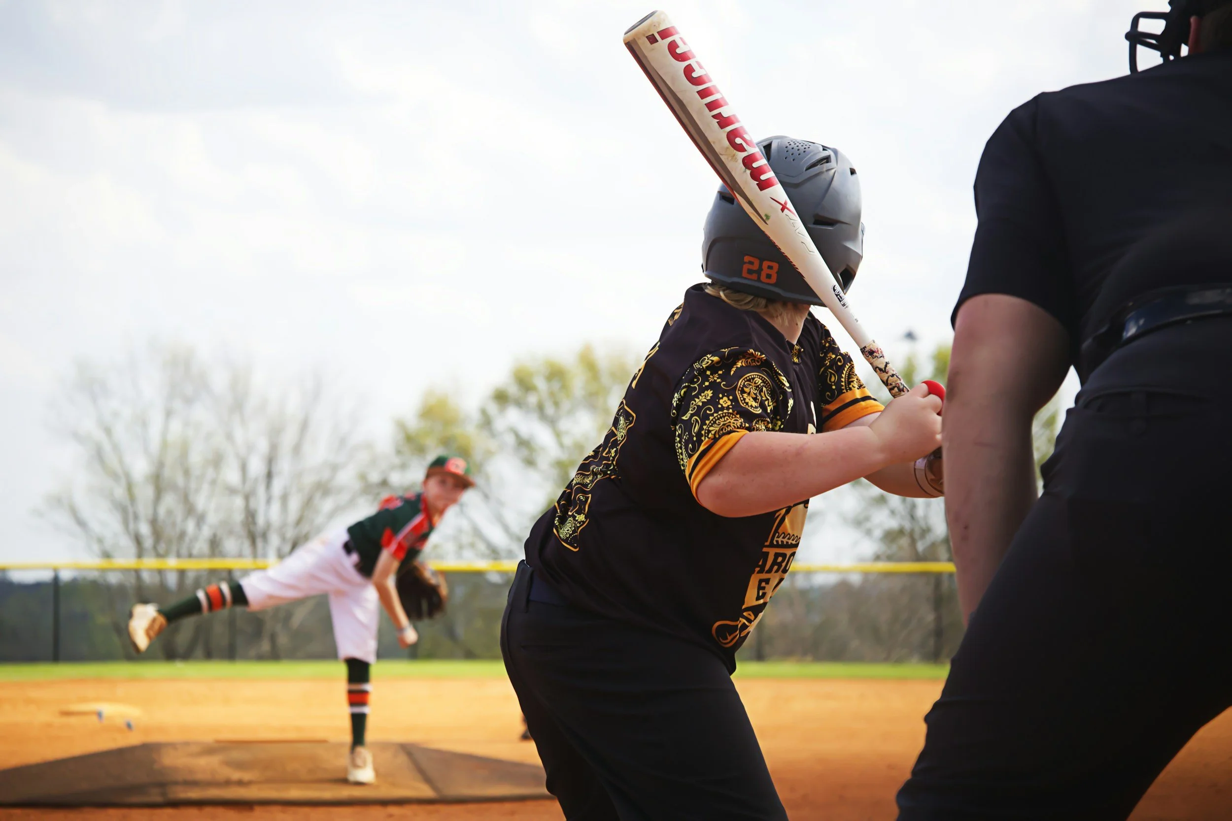 A girl holding a baseball bat engaged in a baseball game, with a player in the background preparing to slide into a base on the field.