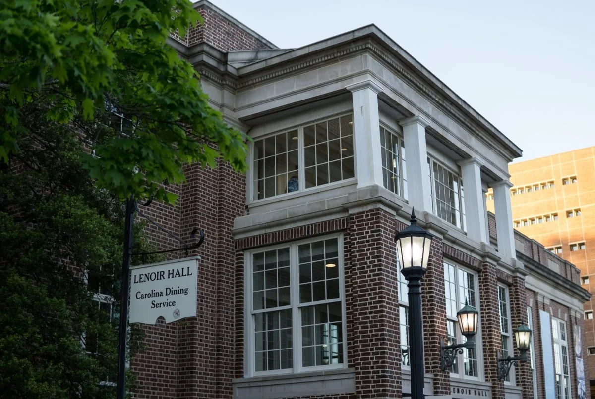 Image of Lenoir Hall, a brick building with white windows and columns, and lamp posts in front, located near Carolina Dining Service.
