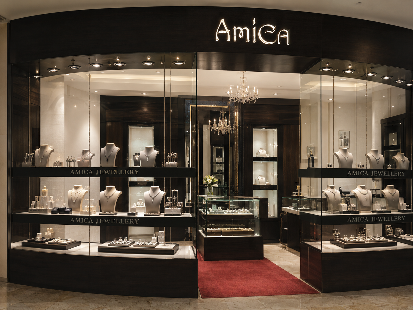 Jewelry store display window with mannequins wearing necklaces and earrings, showcasing the 'Amica Jewellery' brand. Inside the store, jewelry pieces are arranged on shelves and glass cases, illuminated by chandeliers and spotlights.