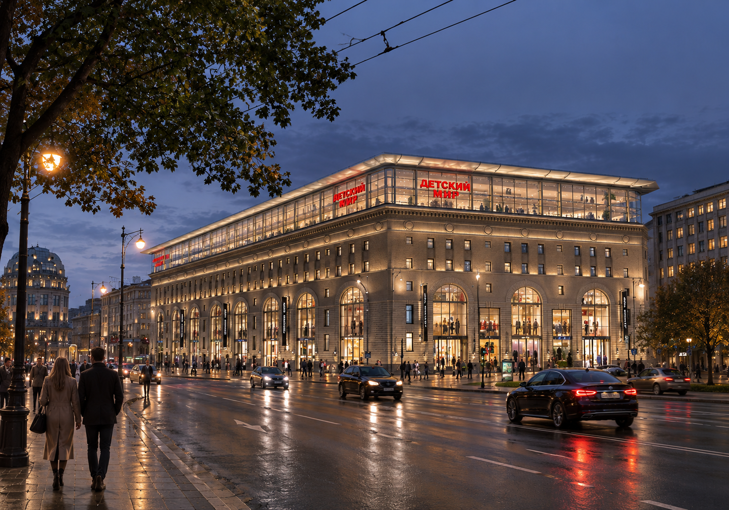 A large multi-story shopping mall illuminated at dusk on a city street with pedestrians and cars. The building has large arched windows, and signs in Russian.