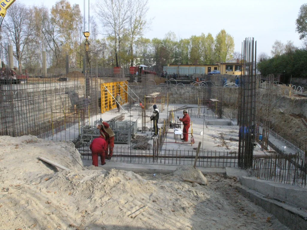 Construction site with workers assembling rebar and pouring concrete for a building foundation.