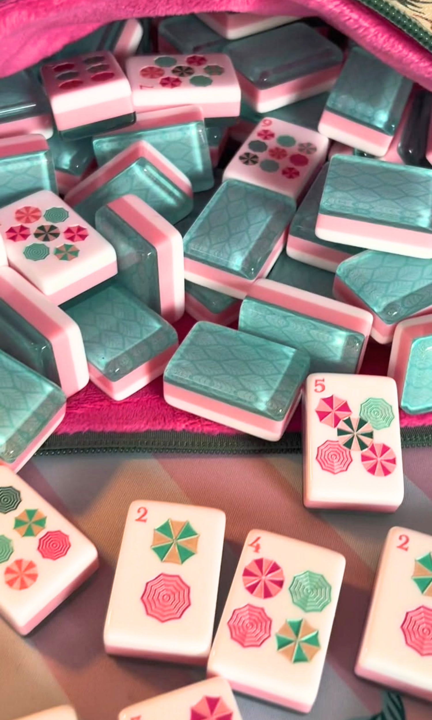 Colorful Mahjong tiles with red, pink, green, and black flower patterns on a game table.