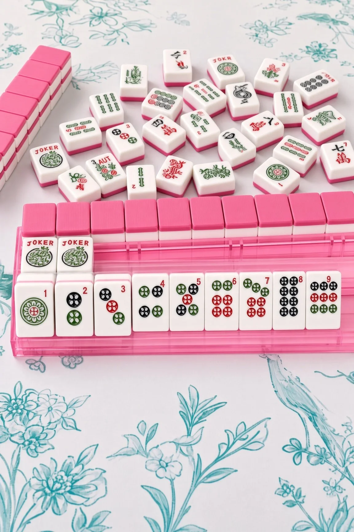 A Mahjong game setup with white and pink tiles on a floral tablecloth.