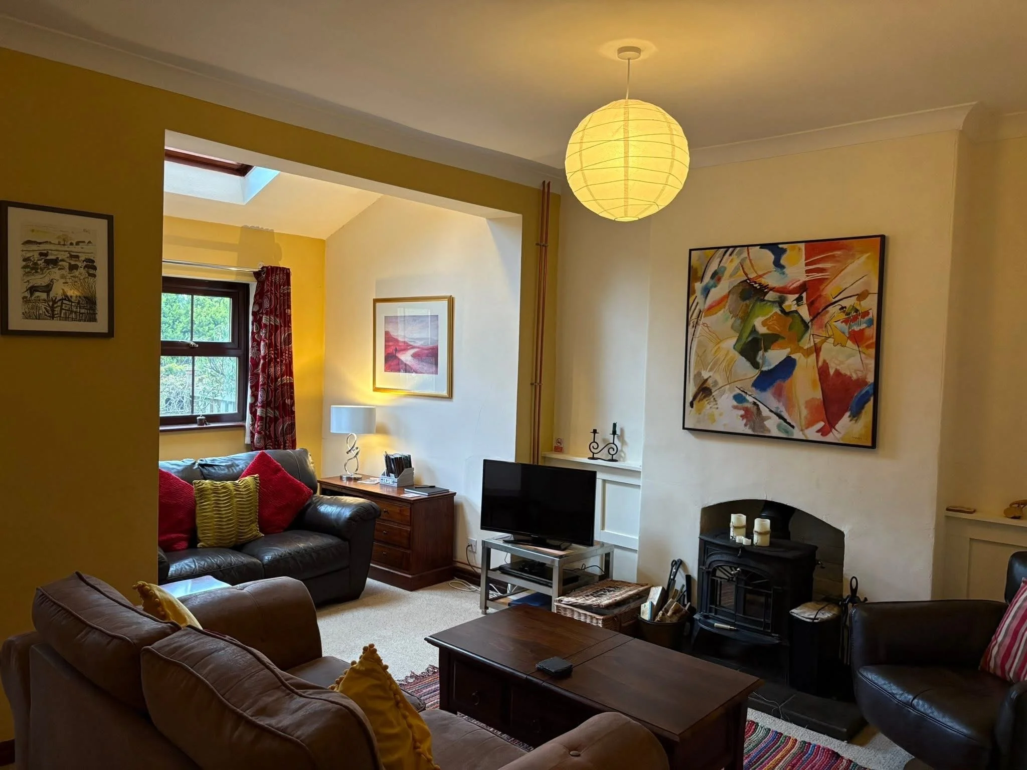 Cozy living room with leather sofas, colorful cushions, fireplace, flat-screen TV, coffee table, pendant light, and abstract wall art