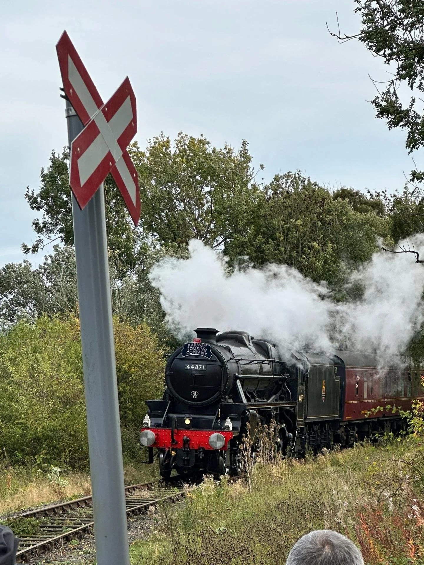 Steam locomotive 44871 hauling passenger cars past a red-and-white railway crossing sign