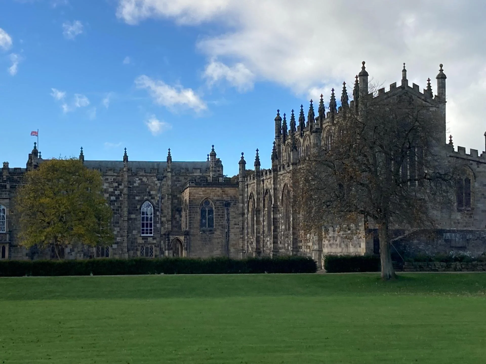 Historic Gothic stone university building with ornate pinnacles and Welsh flag beside a green lawn under a blue sky