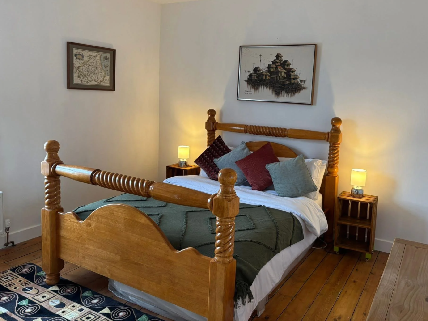 Cozy bedroom with a polished wooden four-poster bed, colorful pillows, bedside lamps, framed artwork, and hardwood floors.