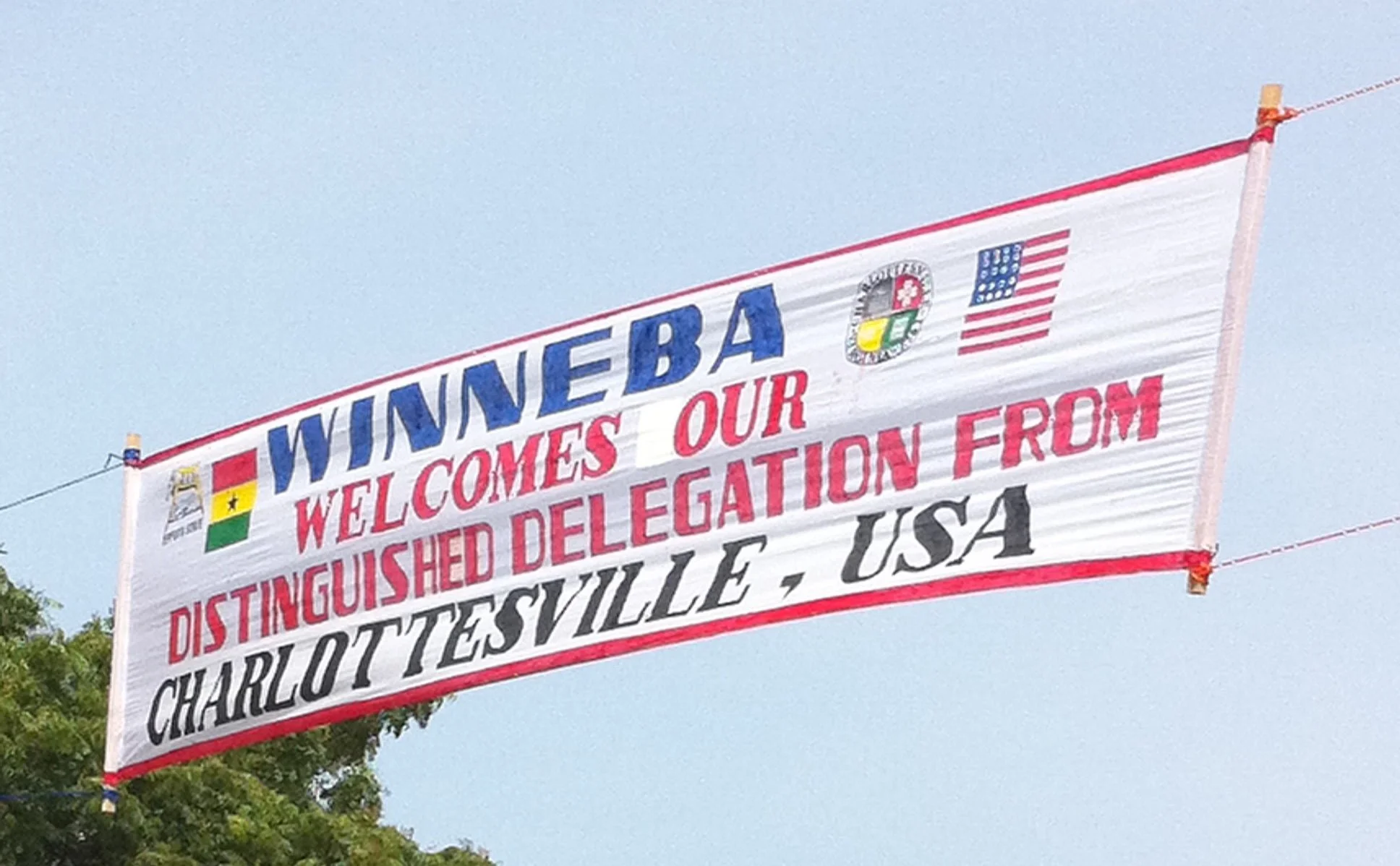 A large outdoor banner with the flags of Ghana and the United States, and text welcoming an American delegation from Charlottesville, Virginia