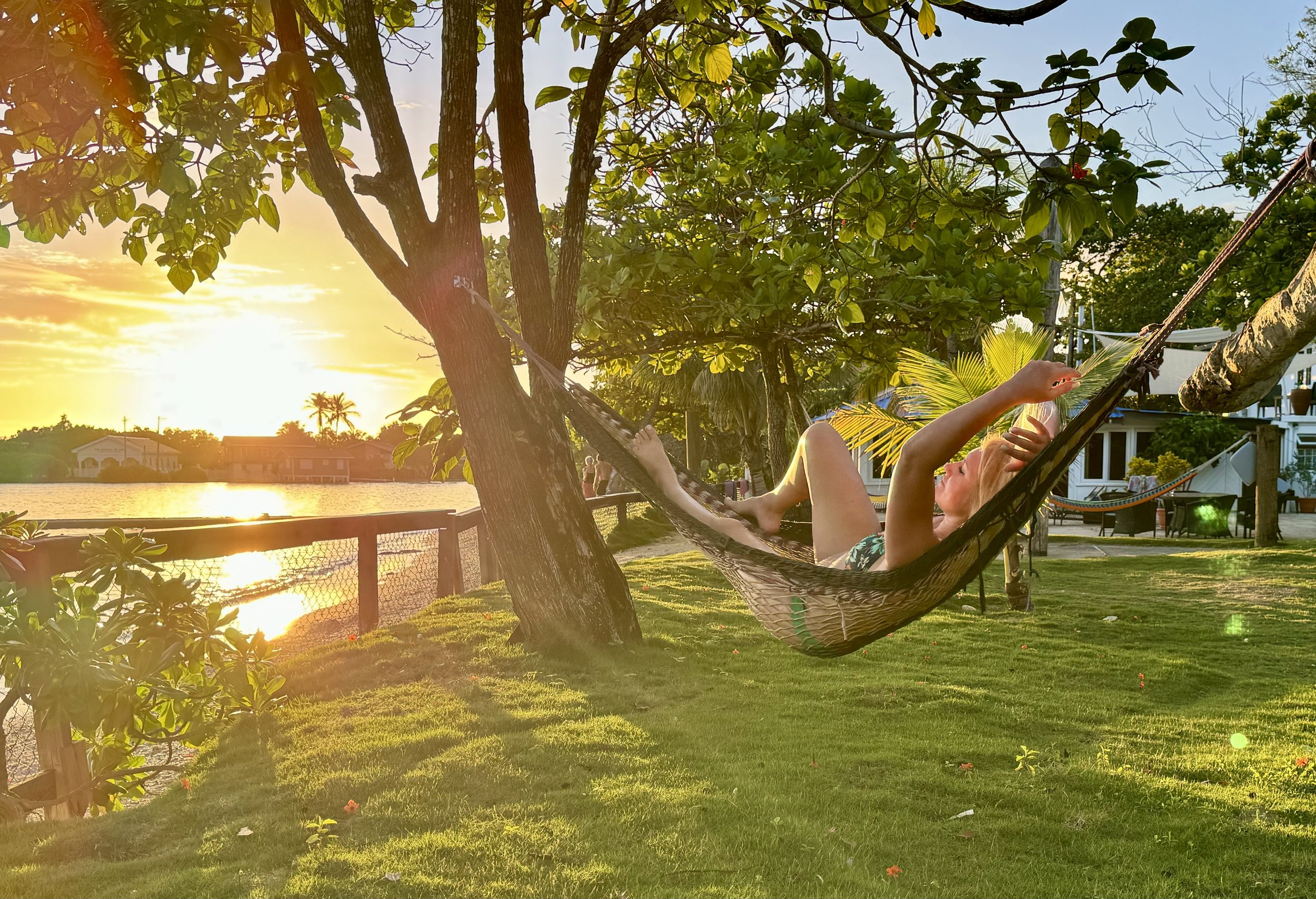 Person relaxing on a hammock tied between trees overlooking the ocean during sunset.