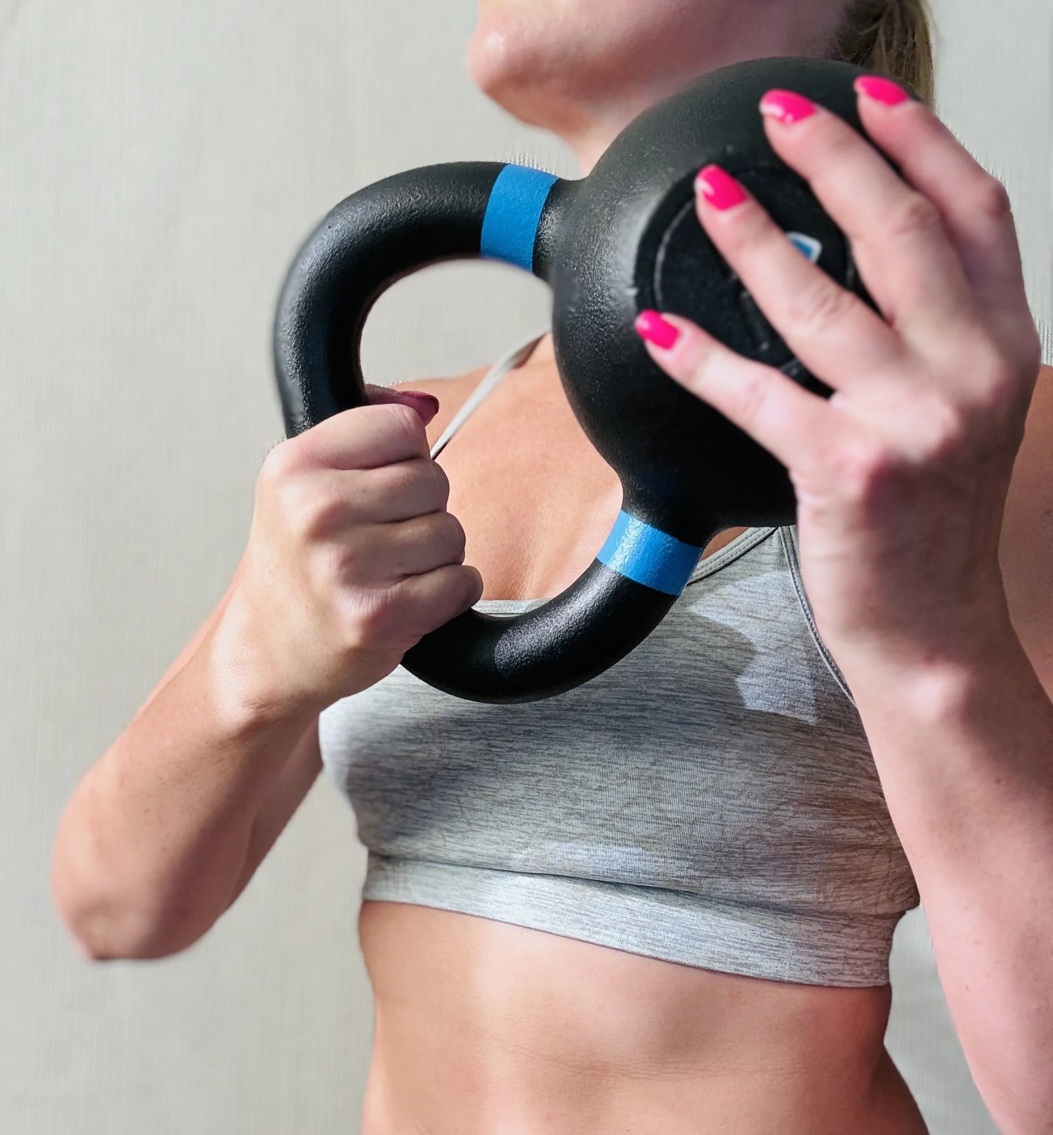 A woman holding a black kettlebell in front of her shoulder, with her other hand gripping the handle.