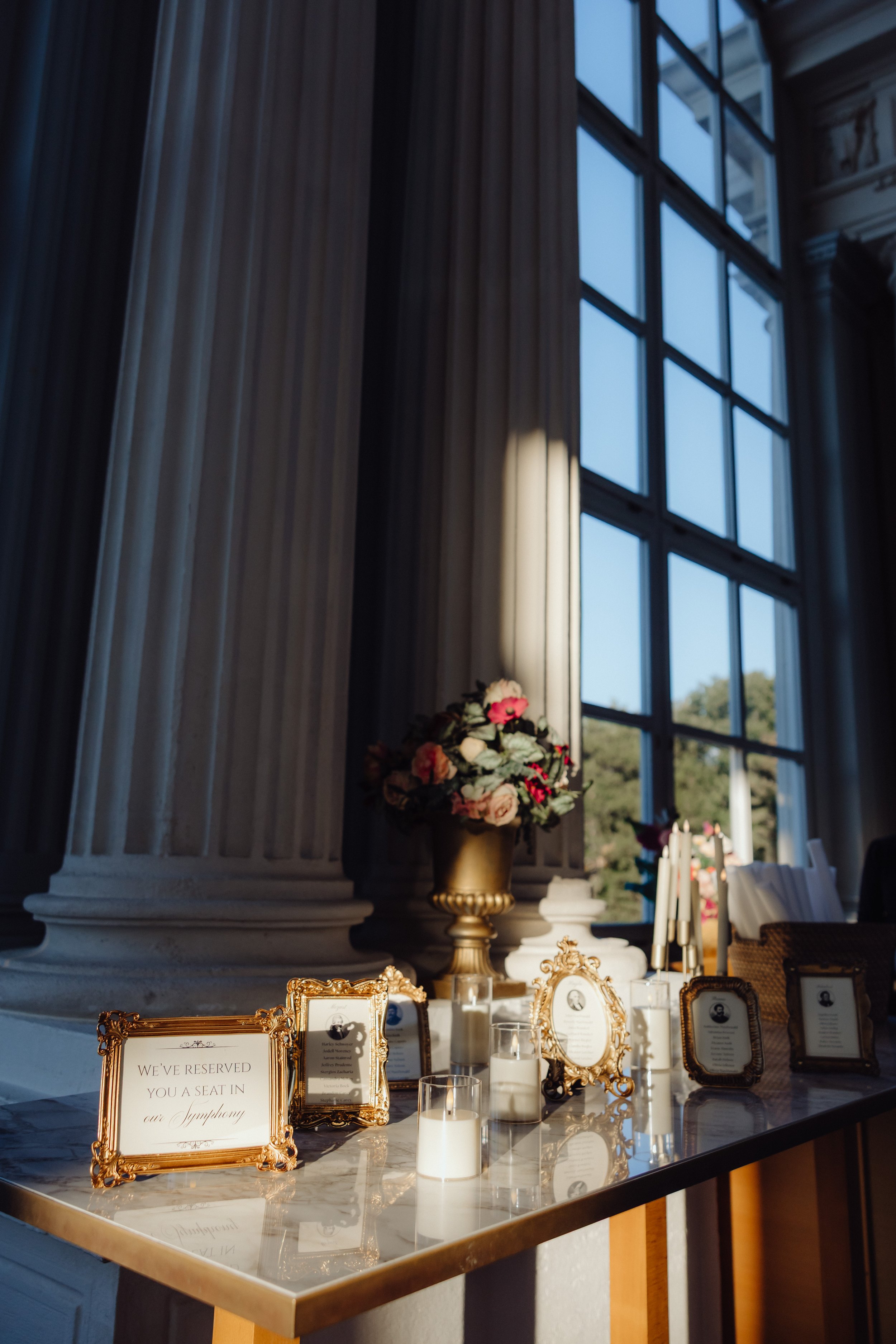 Elegant wedding welcome table featuring gold-framed signs, floral arrangements, and candles inside a historic venue.