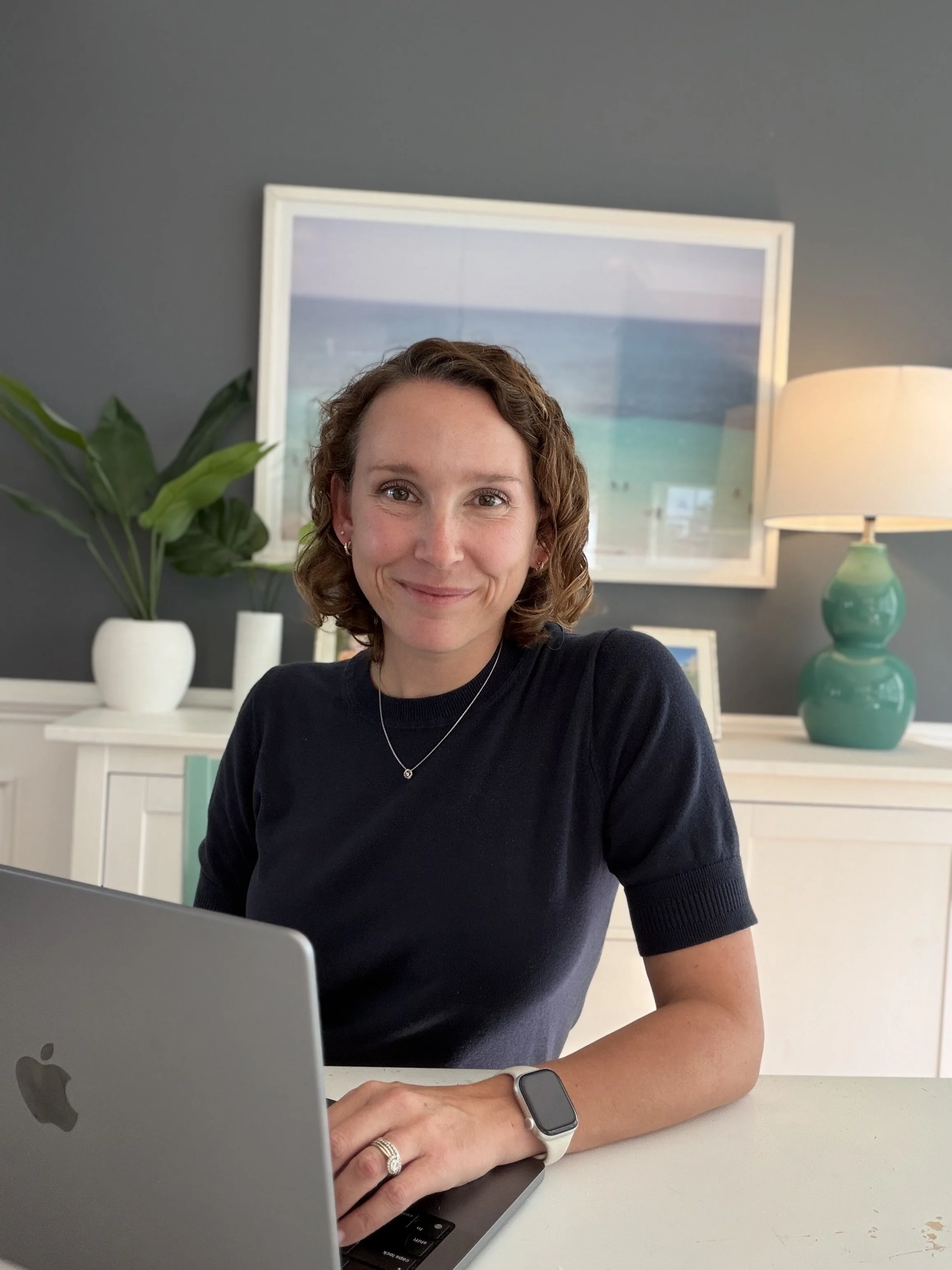 A woman smiles from behind a laptop in a home office