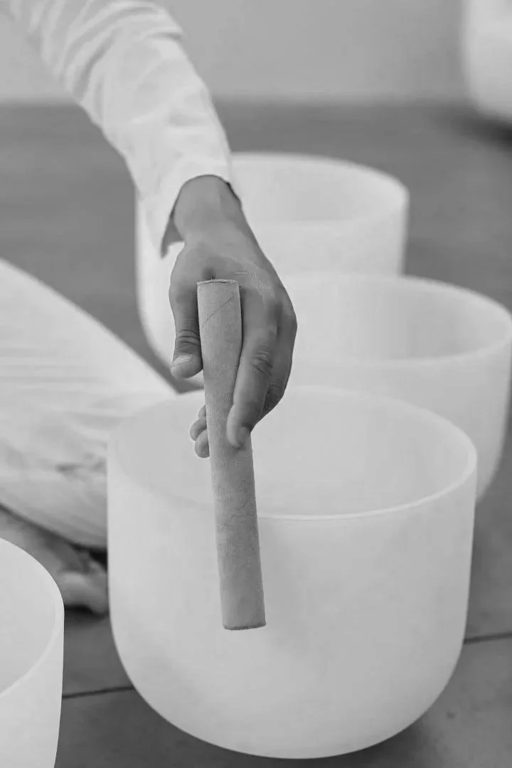 Person playing a set of crystal singing bowls, with a hand holding a mallet hovering above one bowl.