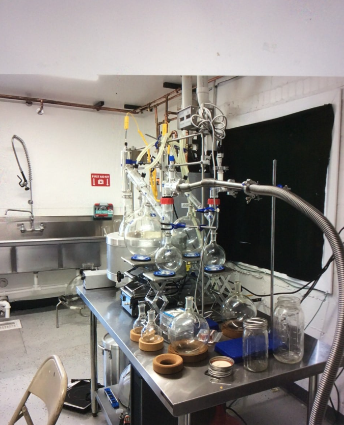 Laboratory setup with glassware and equipment, including glass flasks connected with tubing, jars, and a counter with various laboratory tools, in a scientific research environment.