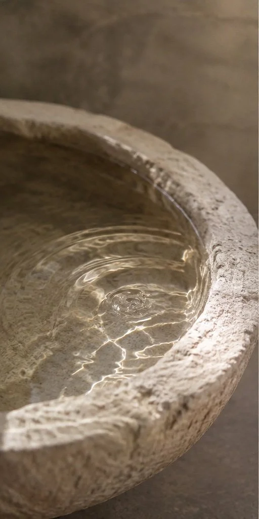 Close-up of a stone fountain with water inside, highlighting the textured stone surface and ripples on the water surface.
