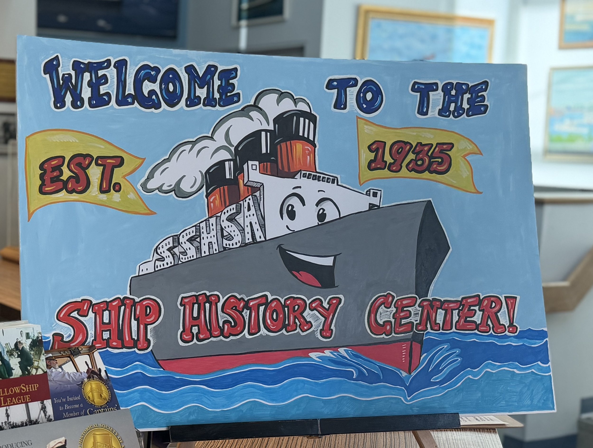 Colorful sign with a cartoon ship and the text "Welcome to the Ship History Center Est. 1935.