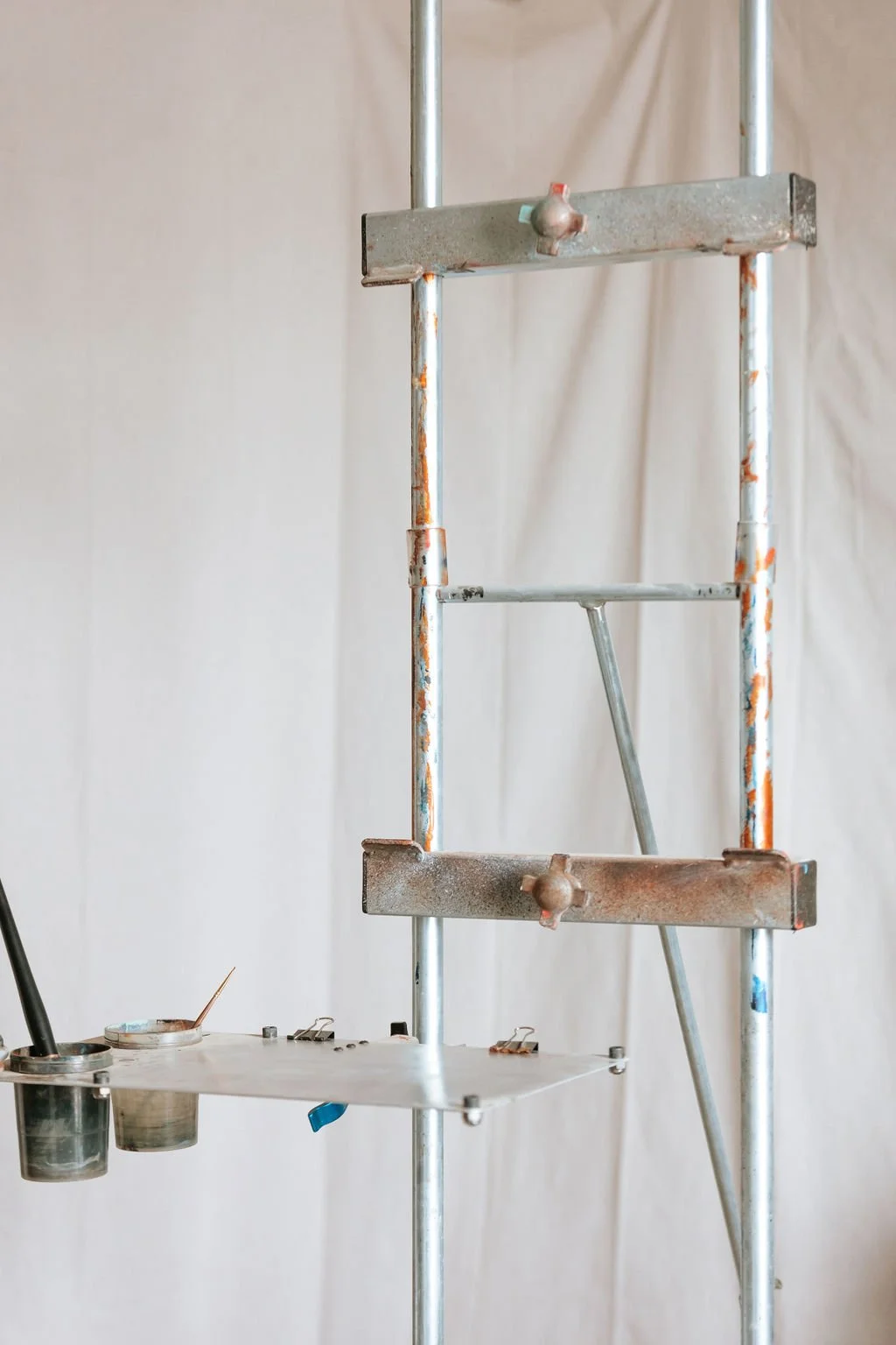 Metal easel with paint supplies and brushes at the bottom, set against a plain background.