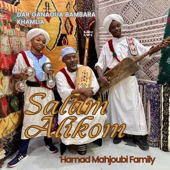 Three members of the Hamad Mahjoub Family dressed in traditional attire, holding musical instruments, standing in front of colorful Moroccan woven rugs and textiles with the text 'Salam Alikom' overlayed.