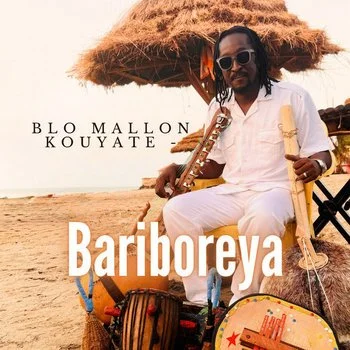 A man with sunglasses and dreadlocks sitting under a thatched umbrella at the beach, holding a wooden flute, with musical instruments and bags around him, and text that reads 'Blo Mallon Kouyate' and 'Bariboreya'.